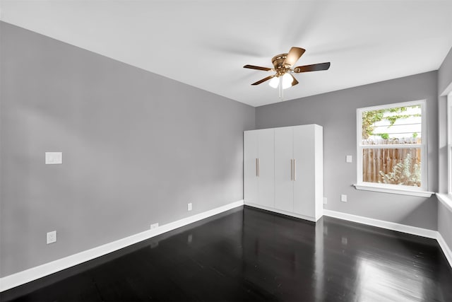 spare room featuring a ceiling fan, dark wood-type flooring, and baseboards