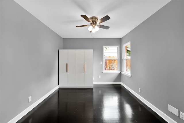 spare room featuring a ceiling fan, baseboards, and dark wood-type flooring