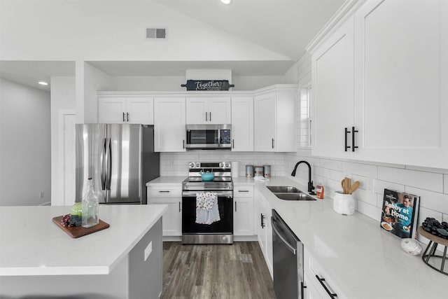 kitchen with vaulted ceiling, sink, appliances with stainless steel finishes, and white cabinetry