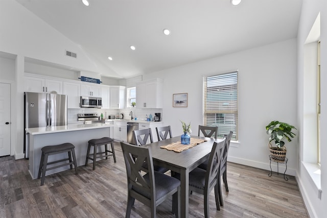 dining area with a healthy amount of sunlight, hardwood / wood-style floors, and high vaulted ceiling