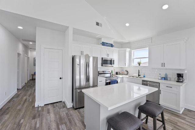 kitchen with a center island, stainless steel appliances, sink, white cabinetry, and lofted ceiling