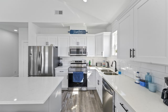 kitchen with hardwood / wood-style floors, vaulted ceiling, sink, appliances with stainless steel finishes, and white cabinets