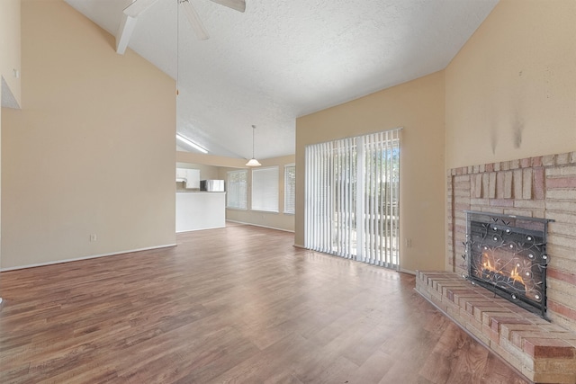 living room with a textured ceiling, a fireplace, hardwood / wood-style floors, high vaulted ceiling, and ceiling fan