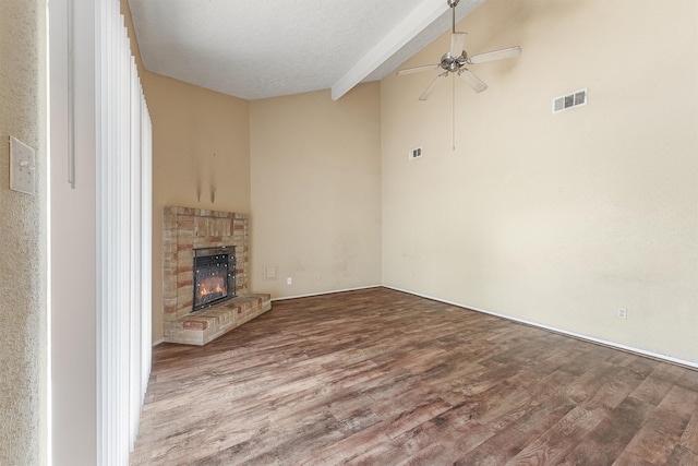 unfurnished living room featuring a textured ceiling, light hardwood / wood-style floors, a brick fireplace, ceiling fan, and vaulted ceiling with beams