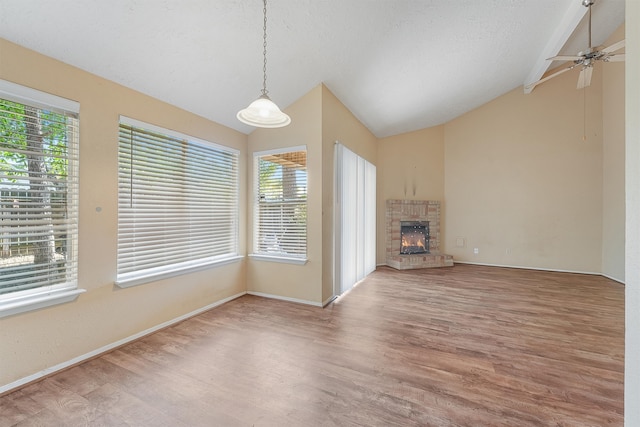 unfurnished living room with a textured ceiling, a fireplace, hardwood / wood-style floors, ceiling fan, and vaulted ceiling with beams