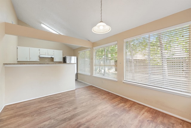 interior space featuring hanging light fixtures, kitchen peninsula, lofted ceiling, light wood-type flooring, and white cabinets