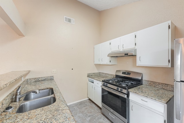 kitchen featuring stainless steel range with gas stovetop, white refrigerator, light stone counters, white cabinetry, and sink