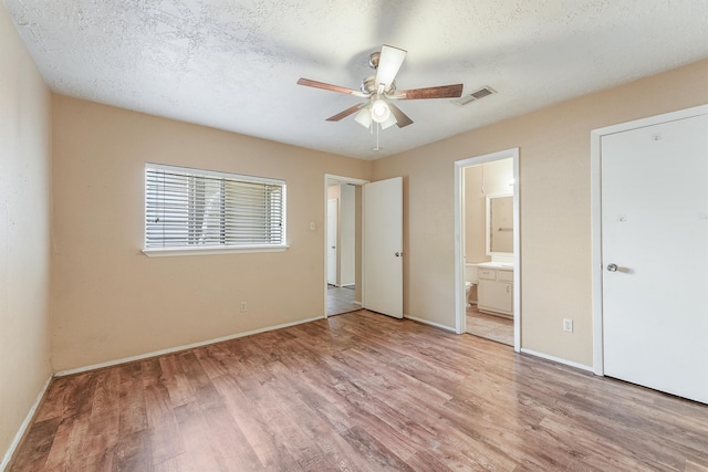 unfurnished bedroom with a textured ceiling, connected bathroom, ceiling fan, and light hardwood / wood-style floors