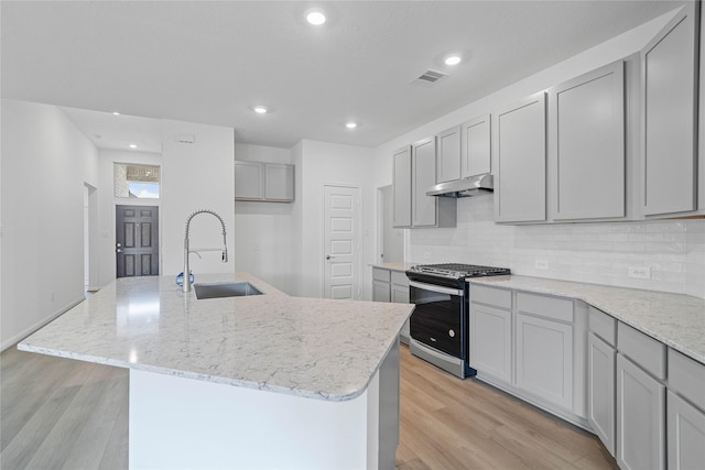 kitchen featuring gas stove, gray cabinets, a kitchen island with sink, and sink