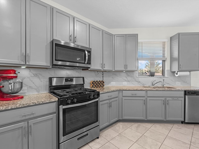 kitchen with gray cabinets, appliances with stainless steel finishes, sink, and light stone countertops