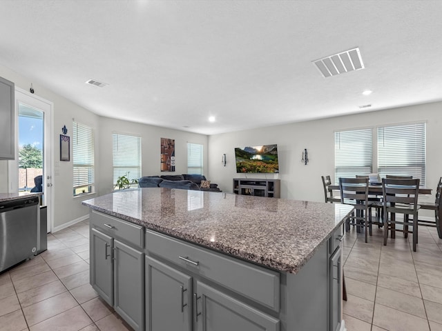 kitchen with stone countertops, a kitchen island, light tile patterned flooring, and stainless steel dishwasher