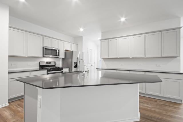 kitchen with dark hardwood / wood-style flooring, a kitchen island with sink, and stainless steel appliances