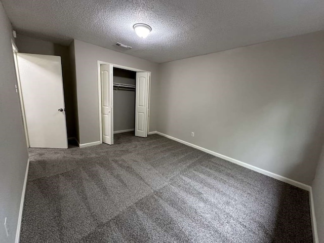 unfurnished bedroom with a textured ceiling, dark carpet, and a closet