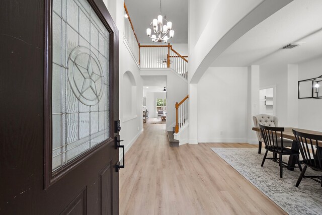 foyer featuring light wood-type flooring, a notable chandelier, and a towering ceiling