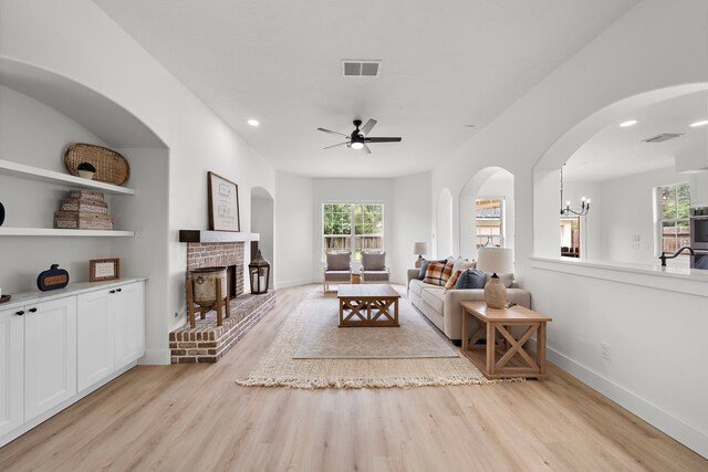 living room with ceiling fan with notable chandelier, a brick fireplace, and light hardwood / wood-style floors