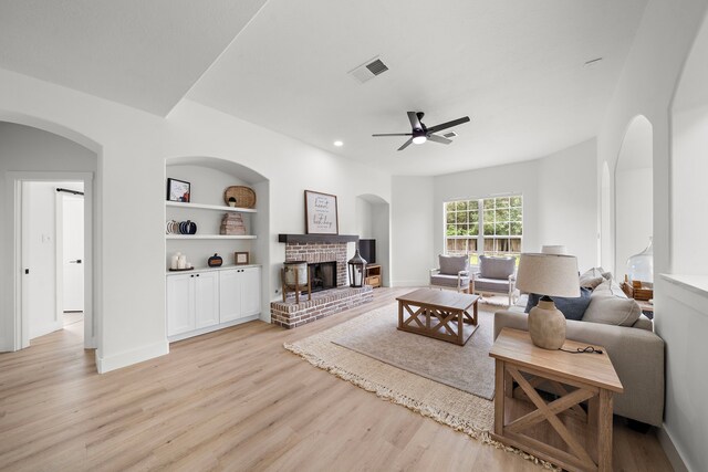 living room with a fireplace, light hardwood / wood-style flooring, built in shelves, and ceiling fan