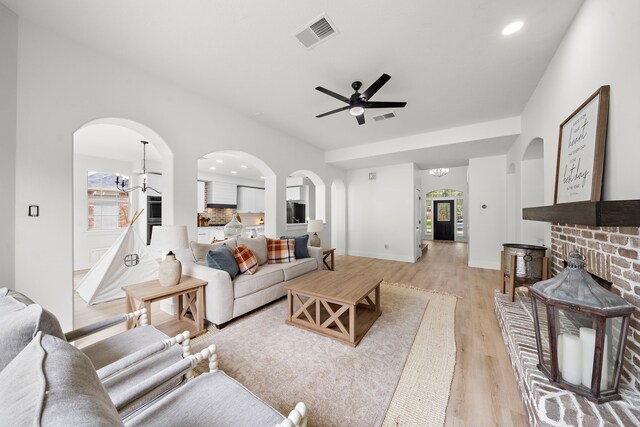 living room featuring ceiling fan with notable chandelier, light wood-type flooring, and a fireplace