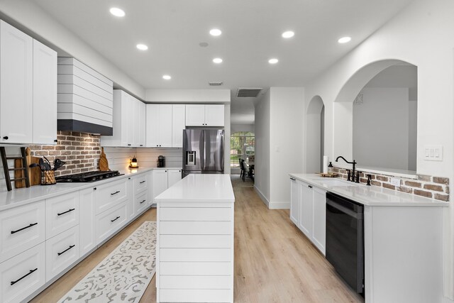 kitchen featuring stainless steel fridge, dishwasher, a kitchen island with sink, sink, and white cabinets