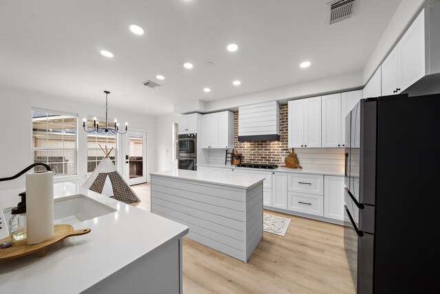 kitchen with decorative light fixtures, black appliances, a kitchen island, and white cabinetry