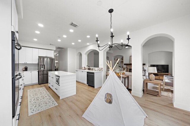 kitchen with a kitchen island, an inviting chandelier, stainless steel appliances, decorative backsplash, and white cabinets