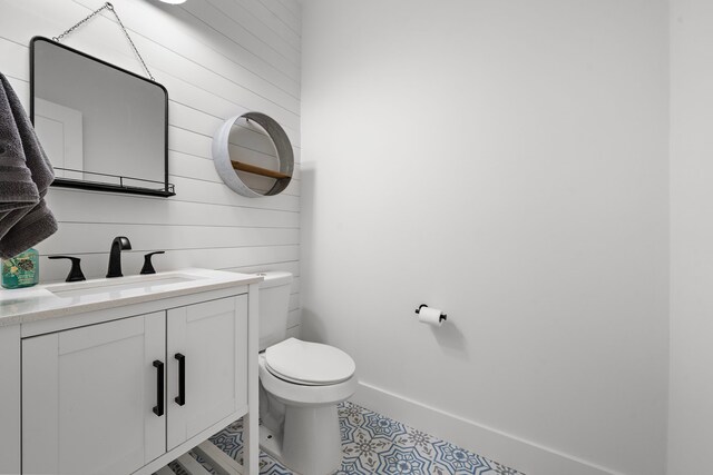 bathroom with vanity, toilet, and wood walls