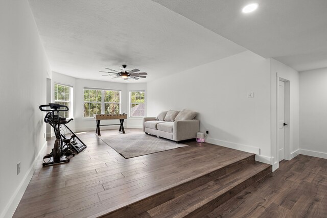 living room with a textured ceiling, ceiling fan, and dark hardwood / wood-style floors