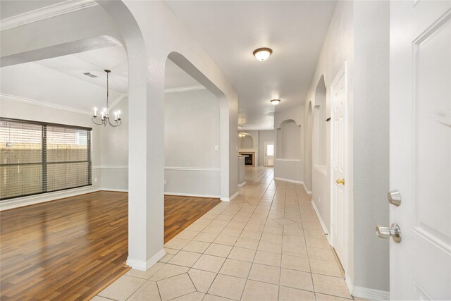 hall featuring light wood-type flooring, an inviting chandelier, and crown molding