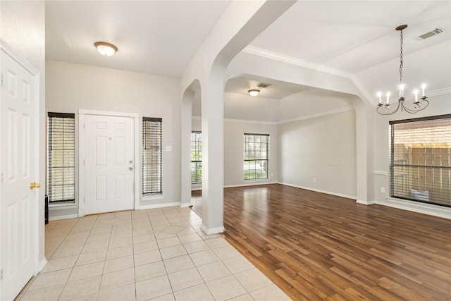 foyer featuring lofted ceiling, a notable chandelier, ornamental molding, and light wood-type flooring