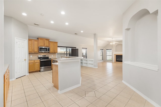 kitchen featuring appliances with stainless steel finishes, light tile patterned flooring, a center island with sink, and ceiling fan