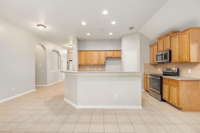 kitchen with stainless steel appliances, a kitchen island with sink, light tile patterned floors, and backsplash