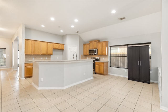 kitchen featuring a kitchen island with sink, backsplash, light tile patterned floors, appliances with stainless steel finishes, and lofted ceiling