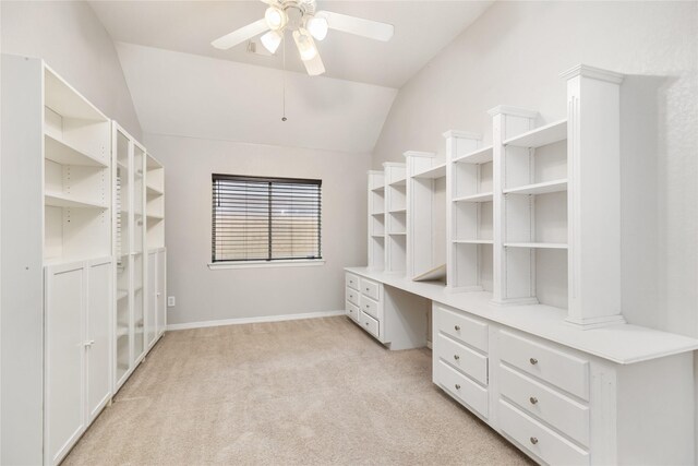 spacious closet with light carpet, built in desk, vaulted ceiling, and ceiling fan