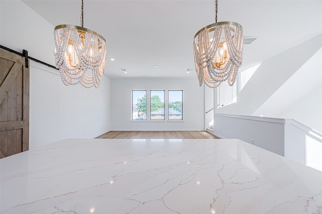 unfurnished dining area featuring light hardwood / wood-style flooring, a notable chandelier, and a barn door