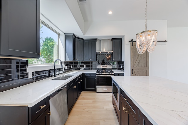 kitchen featuring sink, decorative light fixtures, wall chimney range hood, appliances with stainless steel finishes, and decorative backsplash