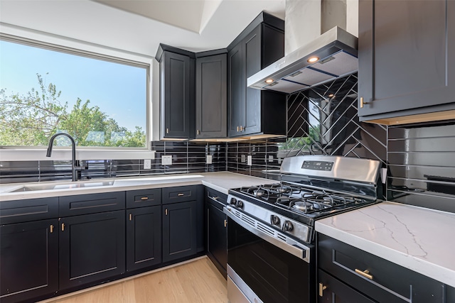 kitchen with light wood-type flooring, sink, wall chimney range hood, backsplash, and gas range