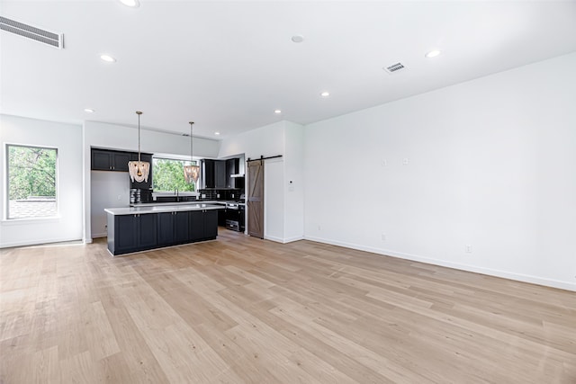 kitchen with light wood-type flooring, sink, a kitchen island, a barn door, and decorative light fixtures