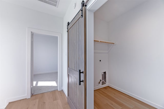 laundry room with a barn door, hookup for a gas dryer, hookup for an electric dryer, and light hardwood / wood-style flooring