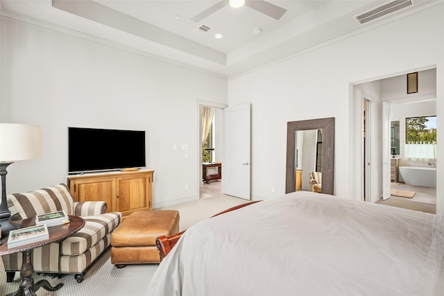 bedroom with ceiling fan, light colored carpet, a raised ceiling, and connected bathroom