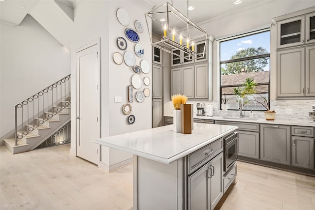 kitchen with a kitchen island, gray cabinetry, pendant lighting, light hardwood / wood-style floors, and stainless steel microwave