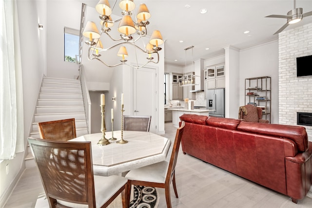 dining space with ceiling fan with notable chandelier, ornamental molding, a fireplace, and light hardwood / wood-style flooring