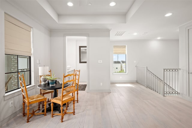 dining room with light wood-type flooring, crown molding, and a tray ceiling