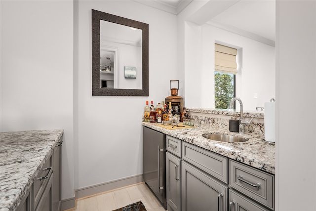 kitchen with gray cabinetry, crown molding, sink, light stone counters, and light wood-type flooring