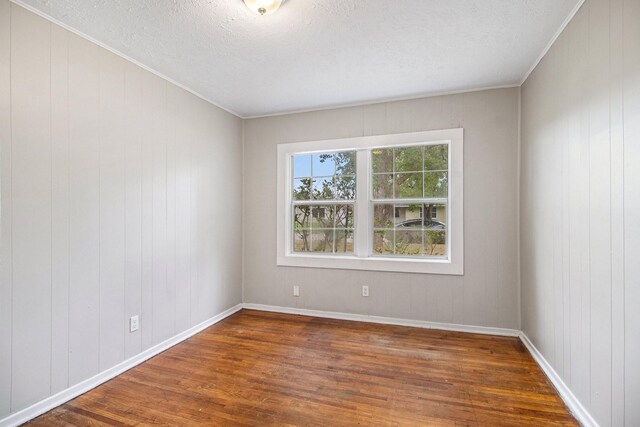 spare room featuring wooden walls, dark hardwood / wood-style flooring, and a textured ceiling