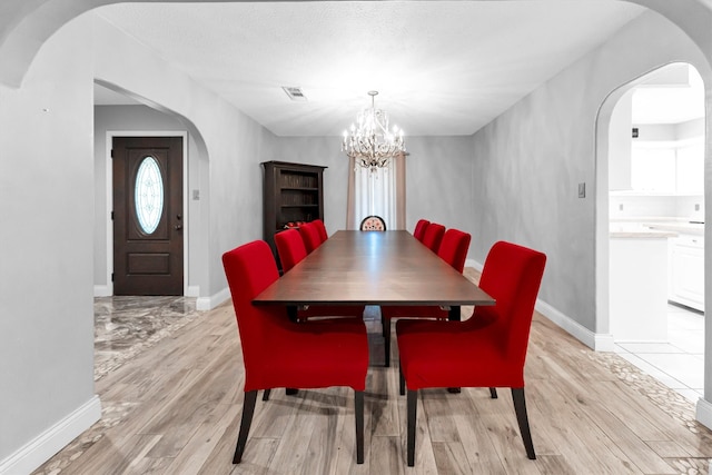 dining area with a textured ceiling, an inviting chandelier, and light hardwood / wood-style floors