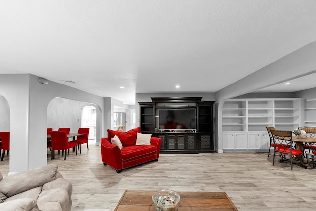 living room featuring built in features, light hardwood / wood-style flooring, and a textured ceiling