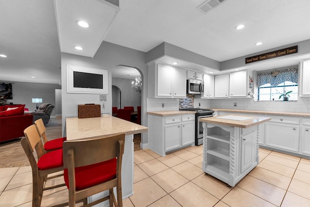 kitchen with white cabinets, backsplash, appliances with stainless steel finishes, light tile patterned flooring, and a kitchen island