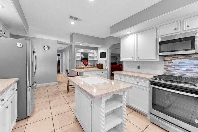 kitchen with appliances with stainless steel finishes, white cabinetry, light tile patterned flooring, a kitchen island, and decorative backsplash