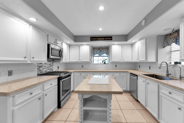 kitchen with light tile patterned floors, a kitchen island, sink, appliances with stainless steel finishes, and white cabinets