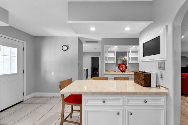 kitchen featuring white cabinetry, light tile patterned flooring, light stone counters, and a kitchen breakfast bar