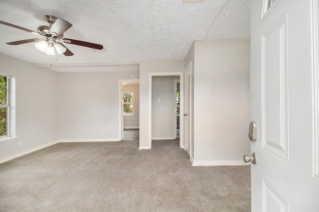 carpeted empty room featuring a textured ceiling, a healthy amount of sunlight, and ceiling fan